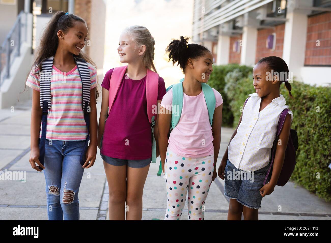 Group of diverse female students with backpacks smiling while looking ...