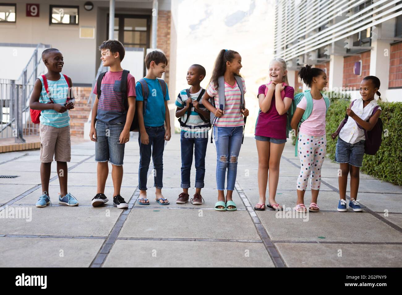 Group of diverse students with backpacks smiling while looking at each other at school Stock Photo