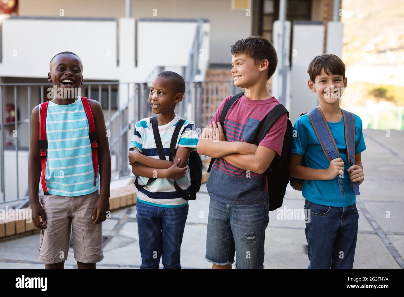 Group of diverse male students with backpacks smiling while standing at school Stock Photo