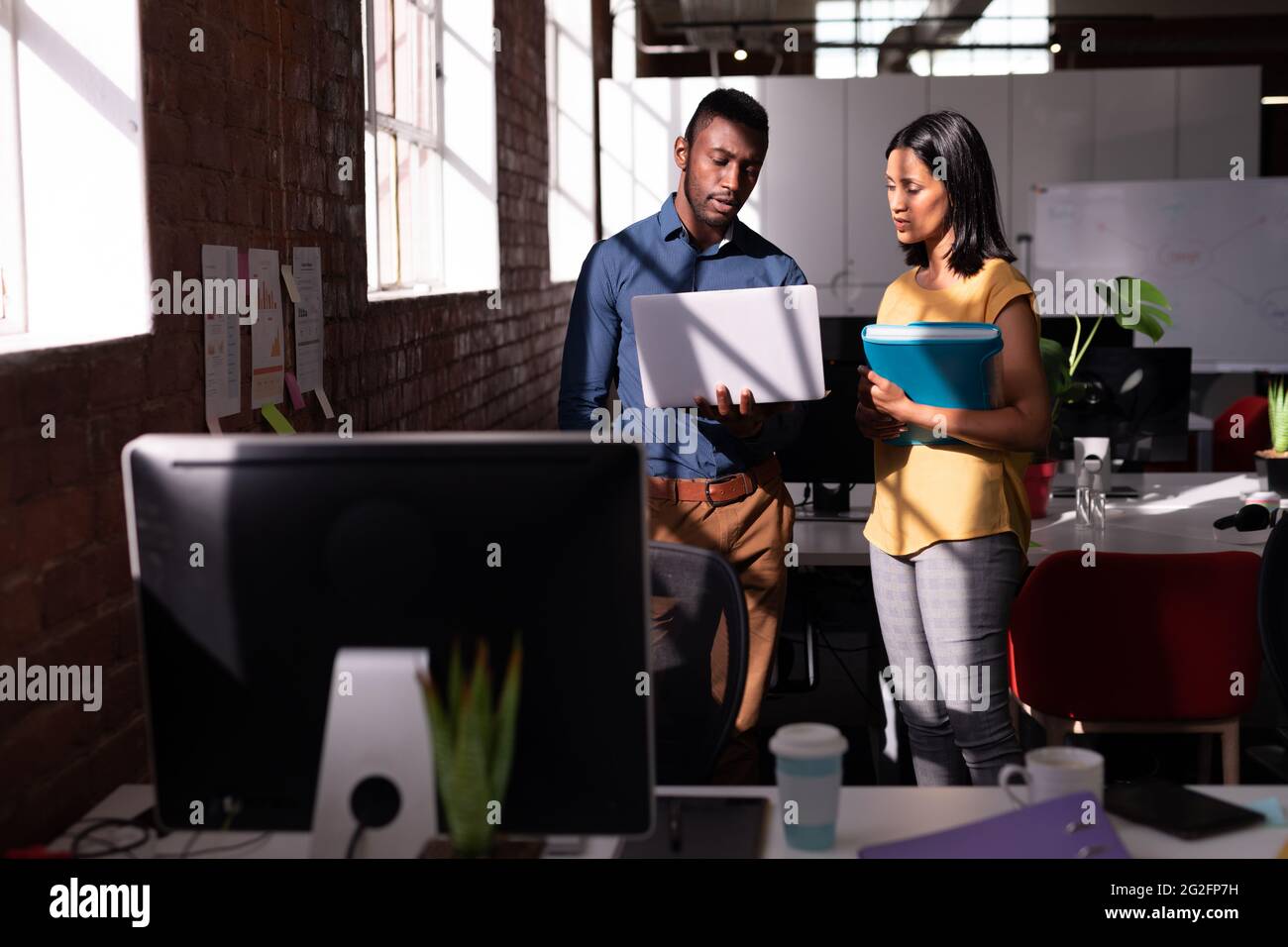 Serious diverse male and female colleague standing in office discussing ...