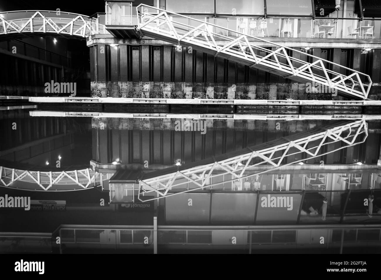 Calm water picks up pier access and apartment reflections in monochrome. Stock Photo
