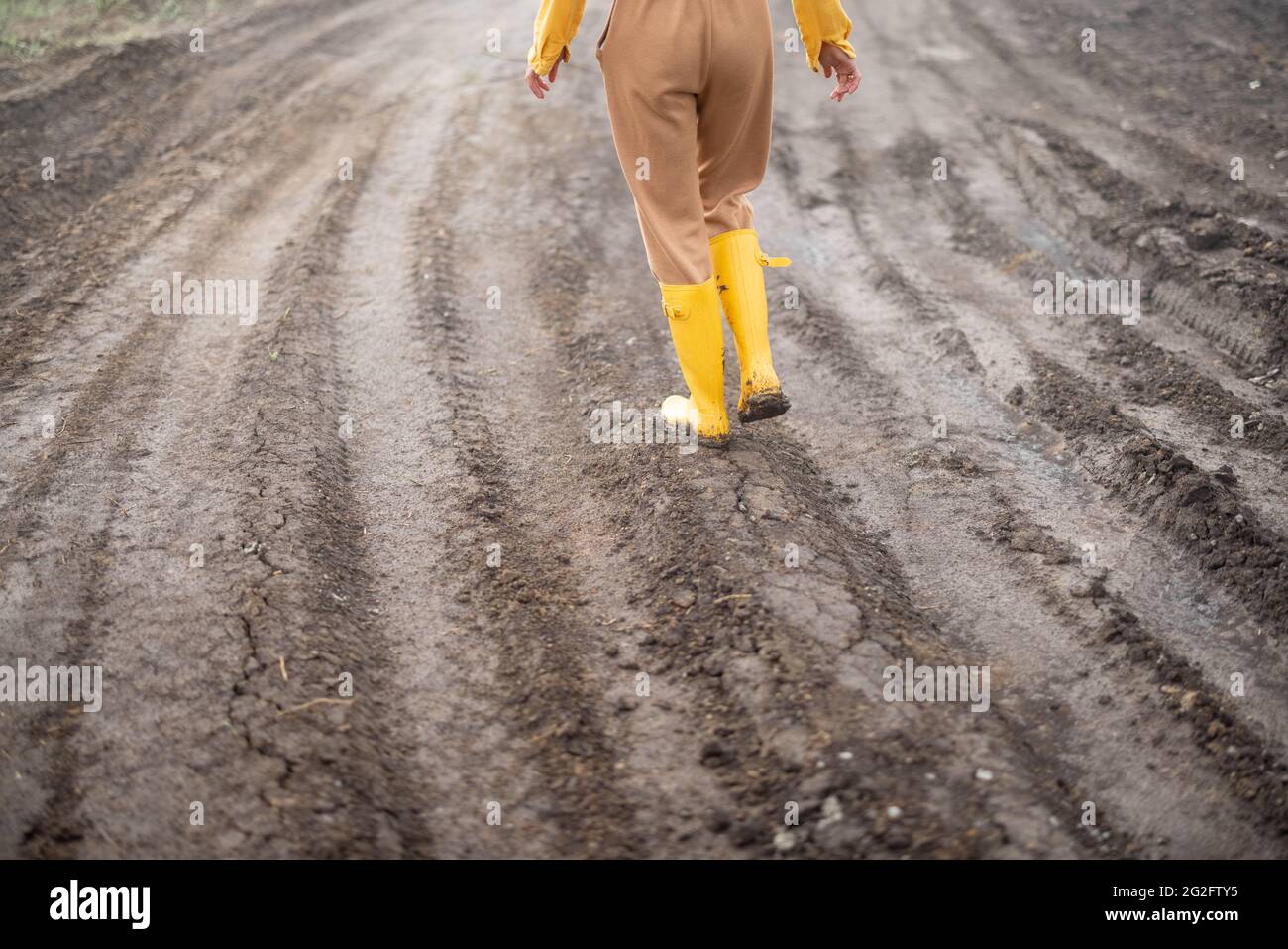Legs of female farmer in yellow rubber boots walking through cultivated agricultural field after the rain.  Stock Photo