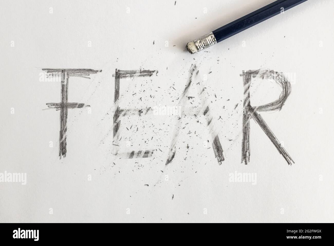 Erasing fear. Fear written on white paper with a pencil, erased with an eraser. Symbolic for overcoming fear or treating fear. Stock Photo