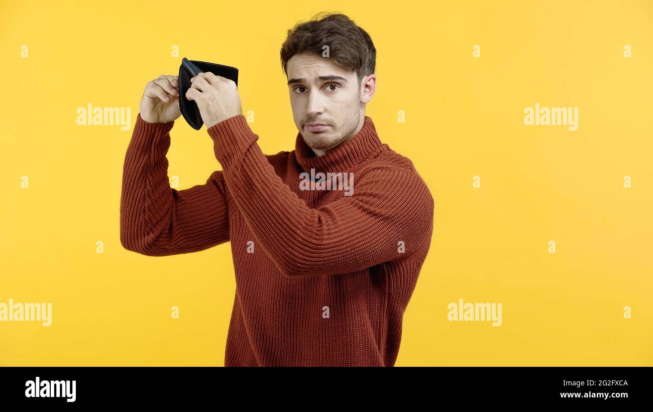 Upset man holding empty wallet isolated on yellow Stock Photo