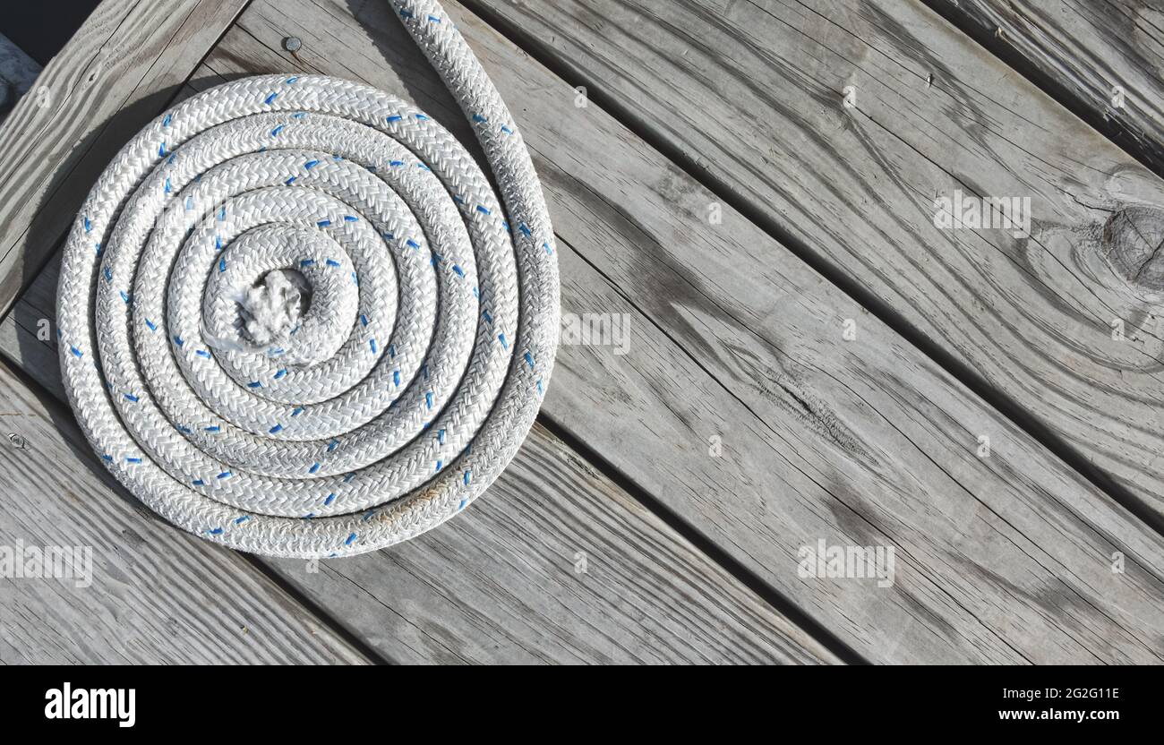 Closeup of a white rope coiled on a weathered wooden dock. Copy space. Stock Photo