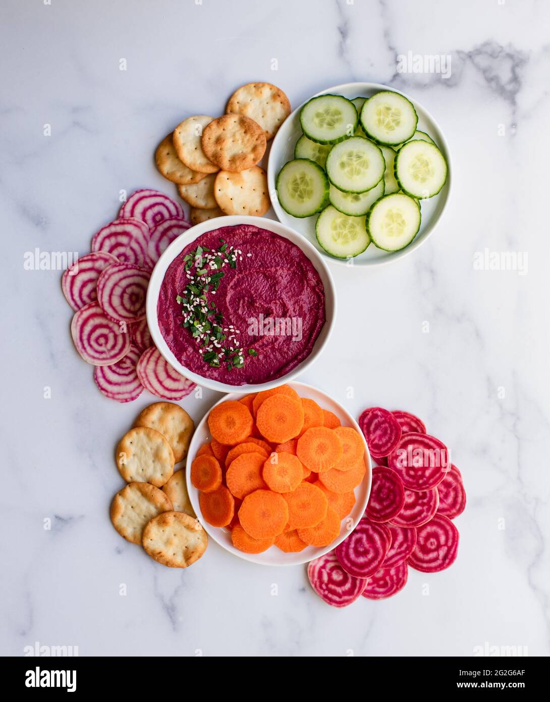 Bowl of beet hummus, vegetables and crackers on white marble counter