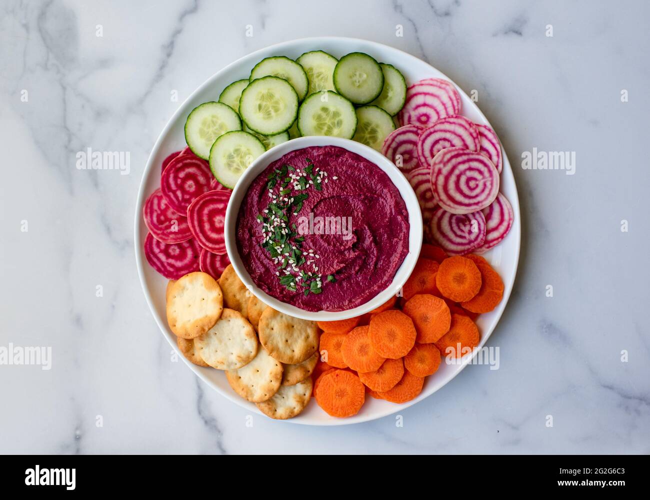 Bowl of beet hummus, vegetables and crackers on white marble counter
