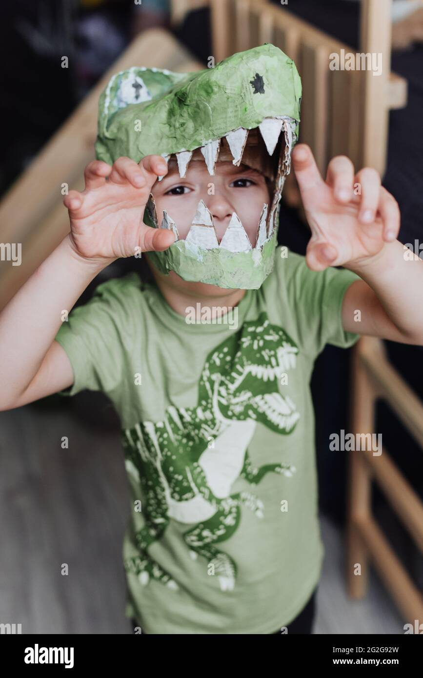 5 years boy playing in his room, wearing green t-shirt with dinosaurus print and t-rex mask Stock Photo