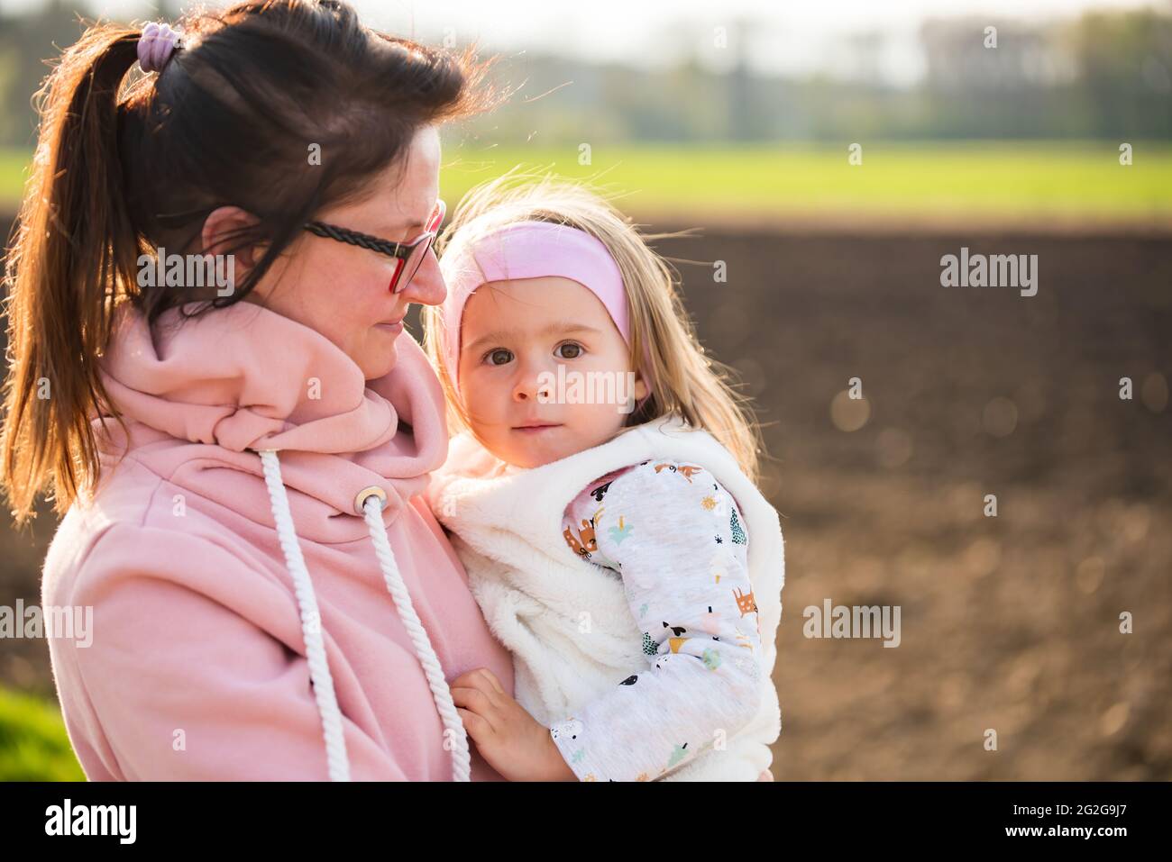 Mother and child walking on countryside road between agricultural fields towards vilage from forest. Stock Photo
