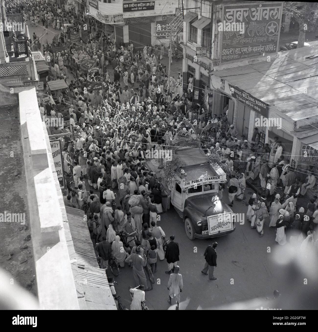 1950s, historical, overhead view of a crowd  of people gathering in a street surrounding an open-ended indian 'public carrier' truck carrying a religious artifact, Benares, India. Stock Photo