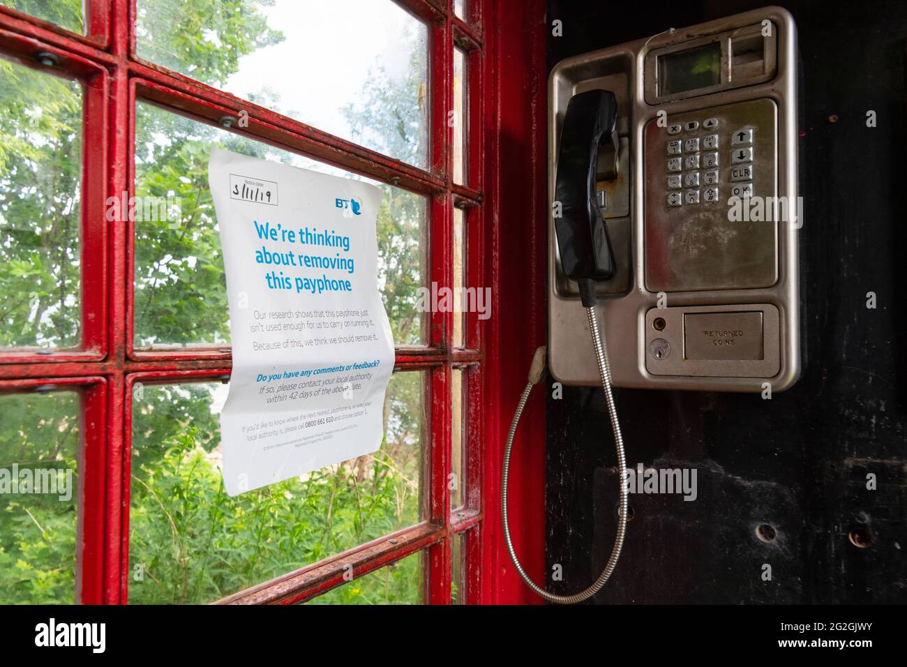 'We're thinking about removing this payphone' notice inside traditional red bt telephone box, Strachur,  Argyll and Bute, Scotland, UK Stock Photo