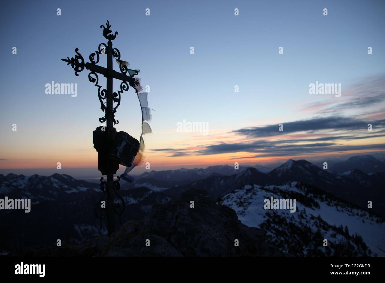 View from the Auerspitz (1811m) towards Chiemgau der Große Traithen (1851m) on the far right, the summit cross in front of the Chiemsee in anticipation of the rising sun, atmospheric, Europe, Germany, Bavaria, Upper Bavaria, Bavarian Alps, Mangfall Mountains, Spitzingsee Stock Photo