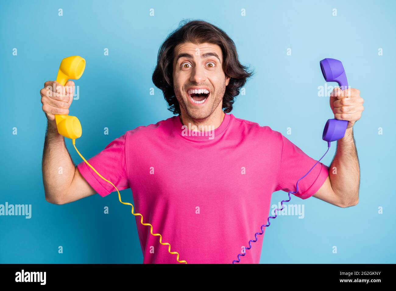 Portrait of attractive cheerful guy holding in hands two handsets having fun consultation isolated over bright blue color background Stock Photo