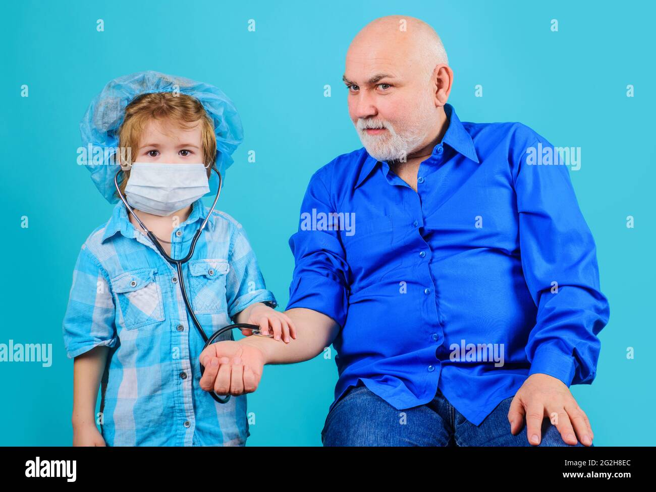 Grandson in medical mask play doctor with grandpa. Medicine. Emergency. Home treatment Stock Photo