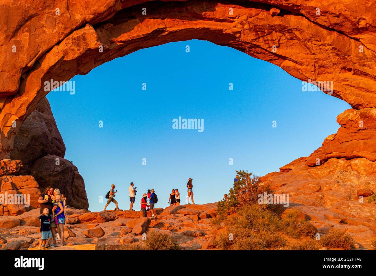 Lots of Tourists standing in the North Window Arch. Arch on the north side of the Windows, a sandstone fin featuring 2 massive, eye-shaped openings in Arches National Park, near Moab in Utah, USA. Stock Photo