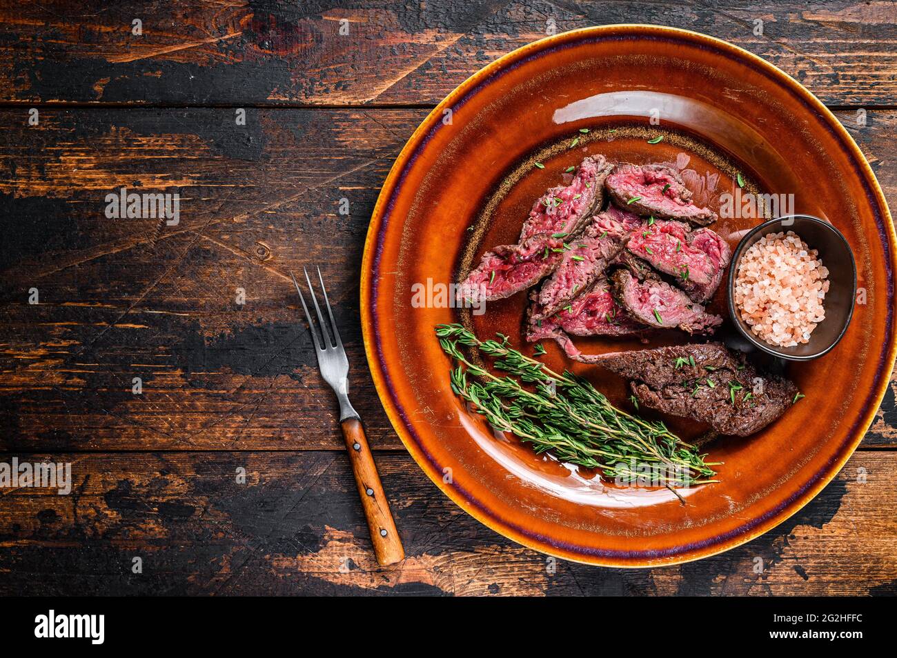 Medium rare Sliced grilled Onglet Hanging Tender meat beef steak on a plate. Dark wooden background. Top view. Copy space Stock Photo