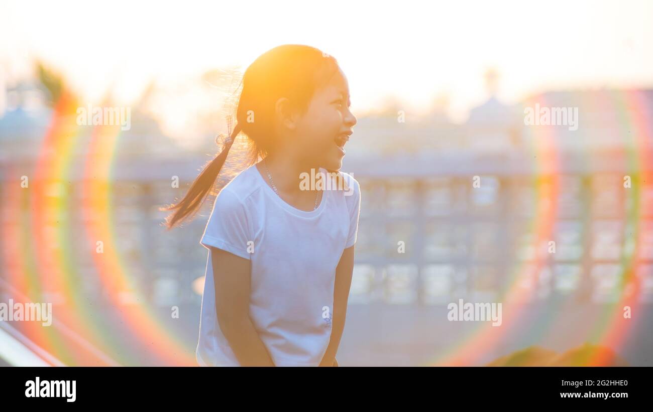 Cute asian child girl smiling with long hair outdoors in summer. Hair flare in the rays of the sunset Stock Photo