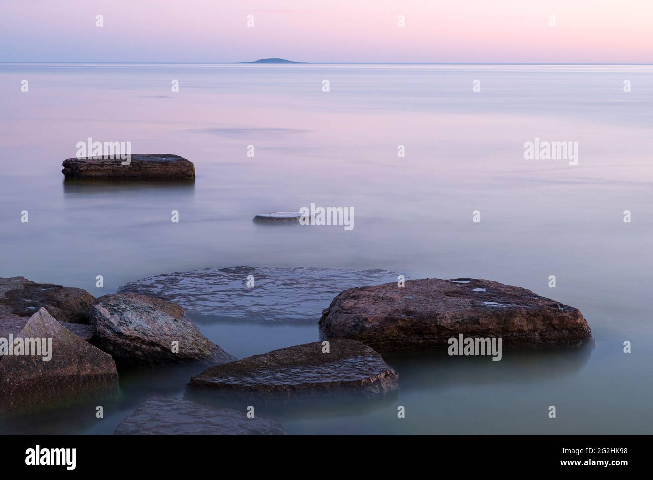 Evening mood on the coast at Byxelkrok, water lapping the stone slabs in the sea, in the background the island of Bla Jungfrun, Sweden, island of Öland Stock Photo