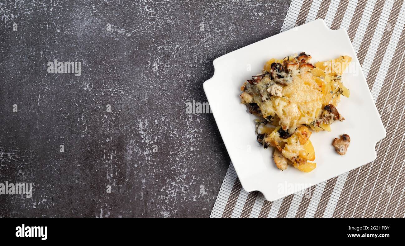 Potato casserole with mushrooms and cheese on a square plate on a dark background. Top view, flat lay Stock Photo