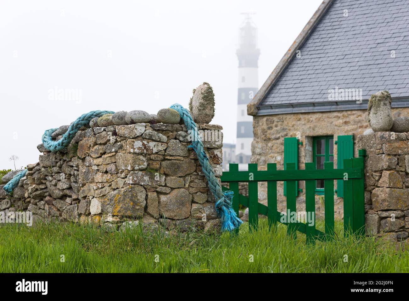 House and stone wall, in the background the lighthouse Créac'h, foggy mood, Île d´Ouessant, France, Brittany, Finistère department Stock Photo