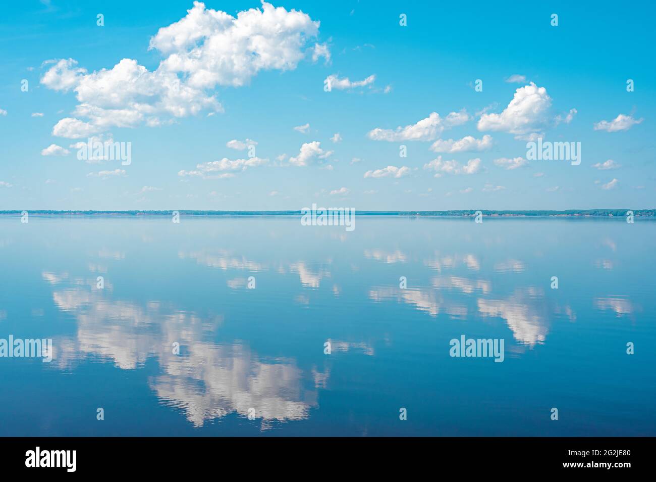 cloudscape. clouds in blue sky and reflection in a large lake. White cumulus clouds in sky over blue sea water. mirror reflection of clouds in lake wa Stock Photo