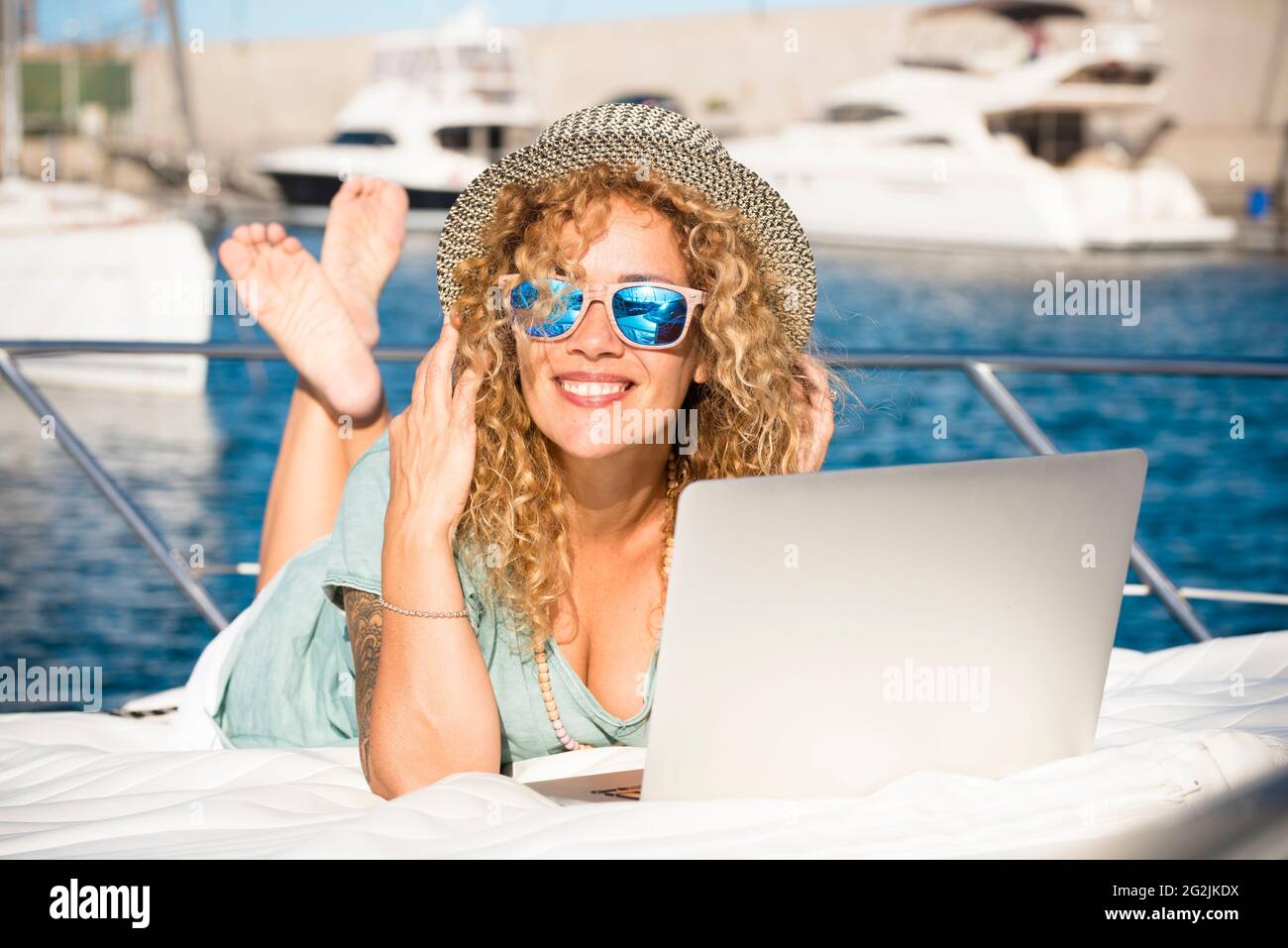 Young pretty adult woman smile and use laptop computer outdoor lay down on the deck of a yacht - travel and summer holiday vacation lifestyle and modern free job - smart working people Stock Photo