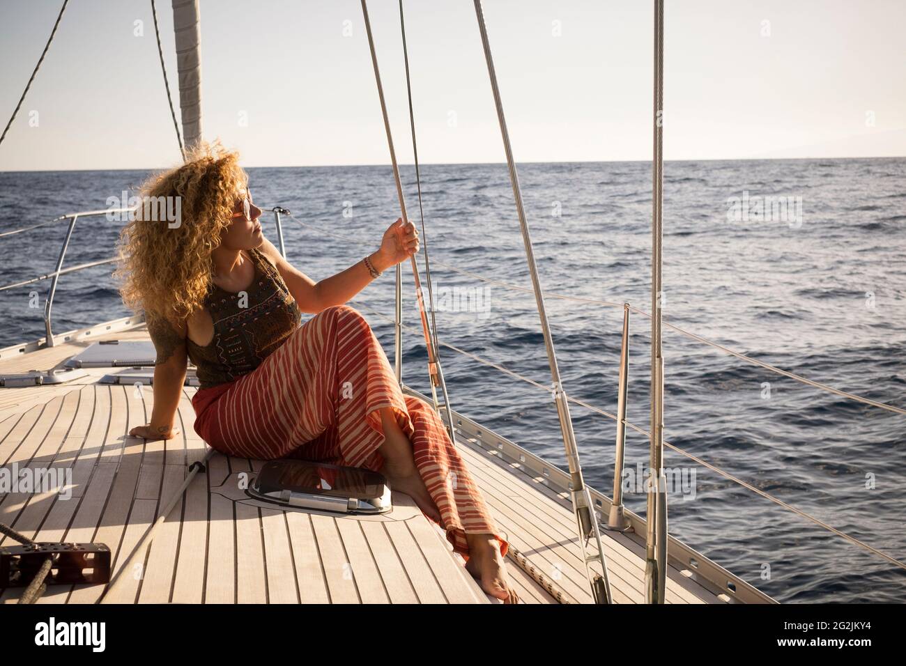 Sail boat travel lifestyle concept with beautiful adult young woman sit down on the deck and enjoy the trip adventure - female people enjoy ocean nature outdoor on the boat Stock Photo