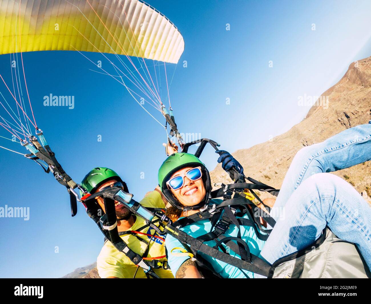 Active young adult people woman enjoy paraglide activity fliying in the sky with professional pilote in the back - cheerful happy female people fly and have fun with paragliding Stock Photo