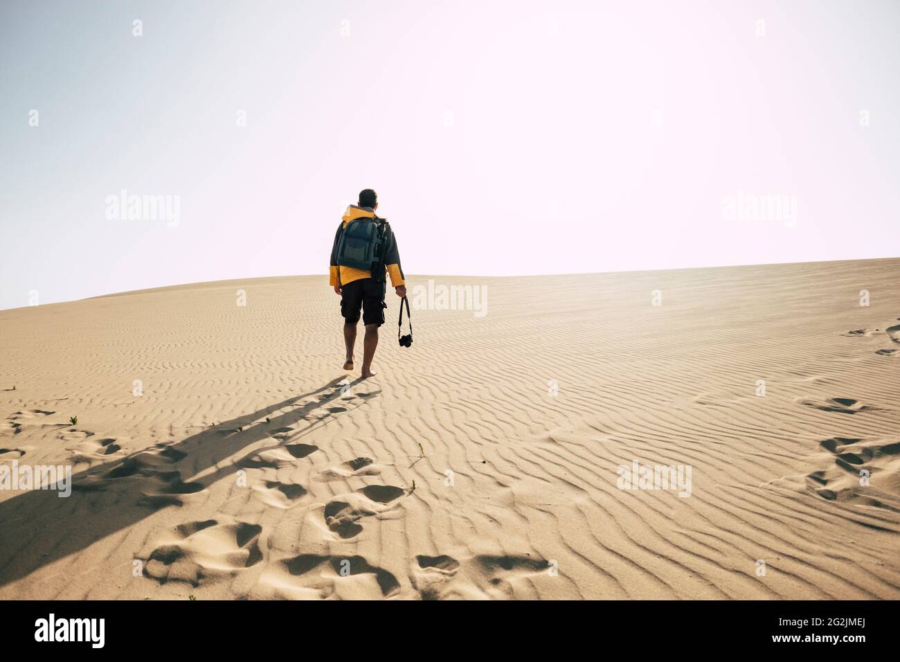 Man walking alone on desert sand dunes - explore and adventure outdoor leisure activity - camera and backpack equipment to enjoy exploration and wild landscape arid place Stock Photo