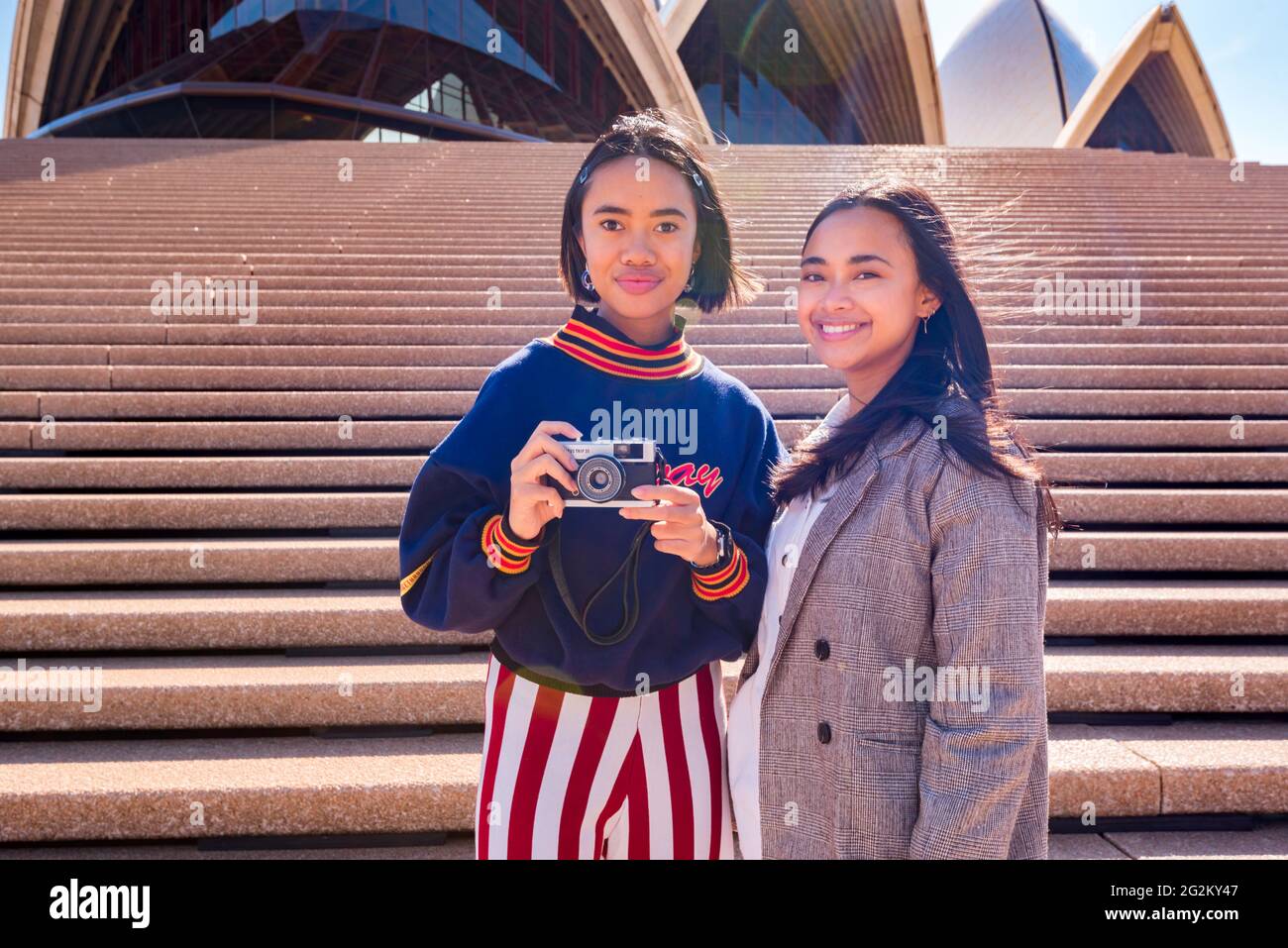 Isabelle and Iris Campbell holidaying in Sydney and taking photos at the Sydney Opera House with their retro Olympus Trip 35mm film camera Stock Photo