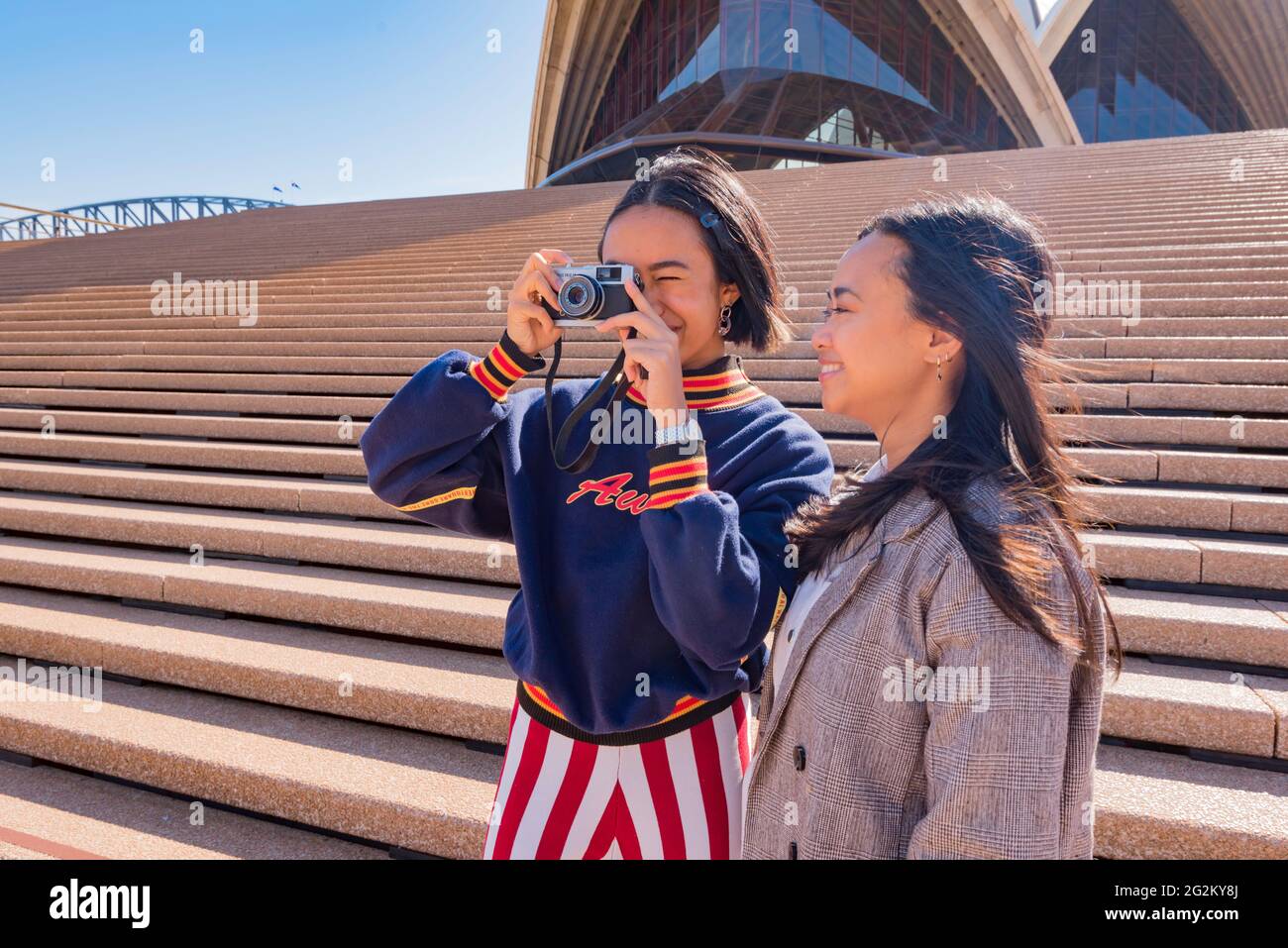 Isabelle and Iris Campbell holidaying in Sydney and taking photos at the Sydney Opera House with their retro Olympus Trip 35mm film camera Stock Photo