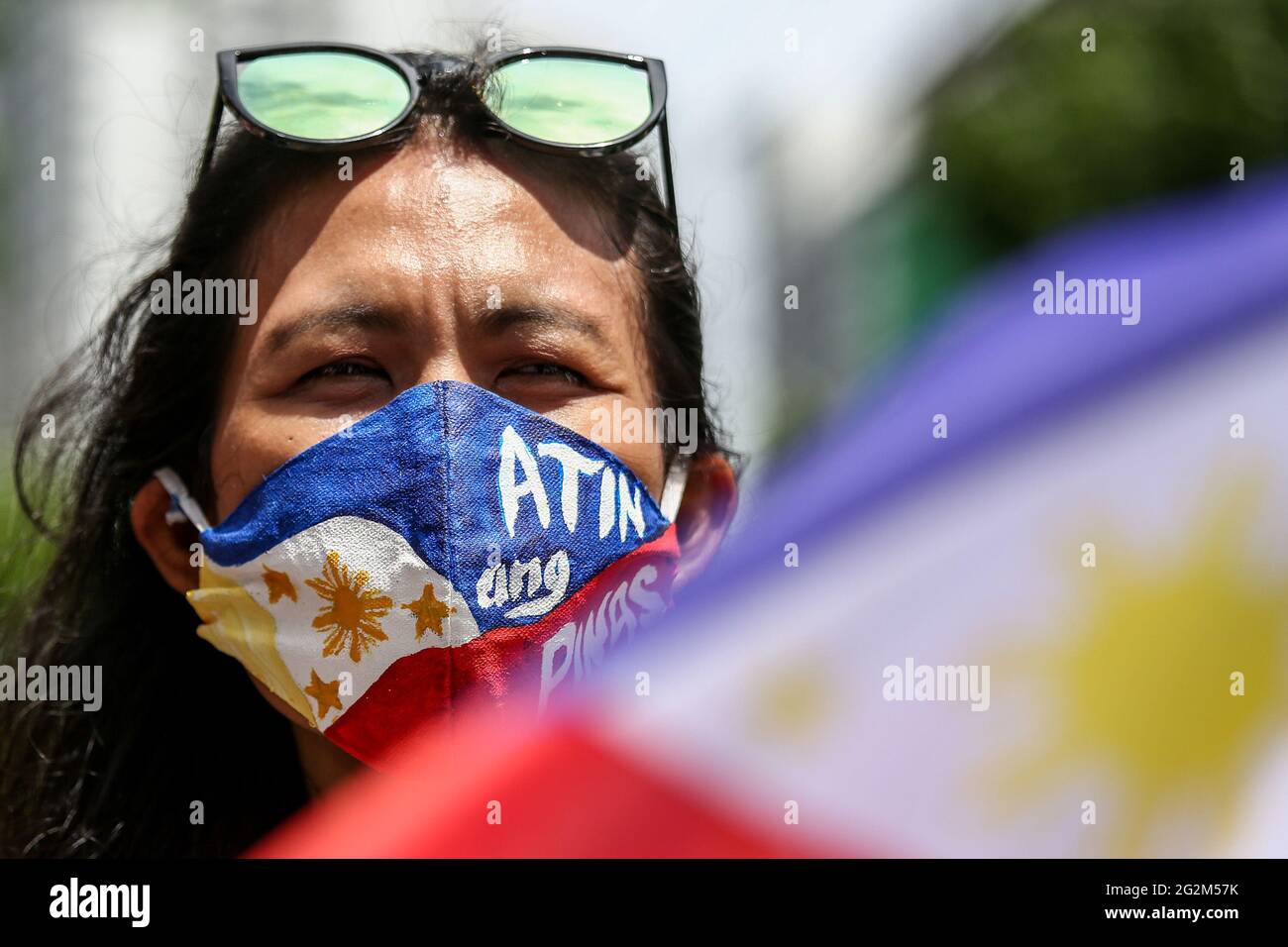 Metro Manila, Philippines. 12th June 2021. A woman wears a mask bearing the Philippine flag with a sign 'Atin Ang Pinas' during a protest marking Independence Day in front of the Chinese consulate in the financial district of Makat. Various groups called on China to stop its maritime activities in the disputed South China Sea, which endangers peace and stability in the region. Credit: Majority World CIC/Alamy Live News Stock Photo