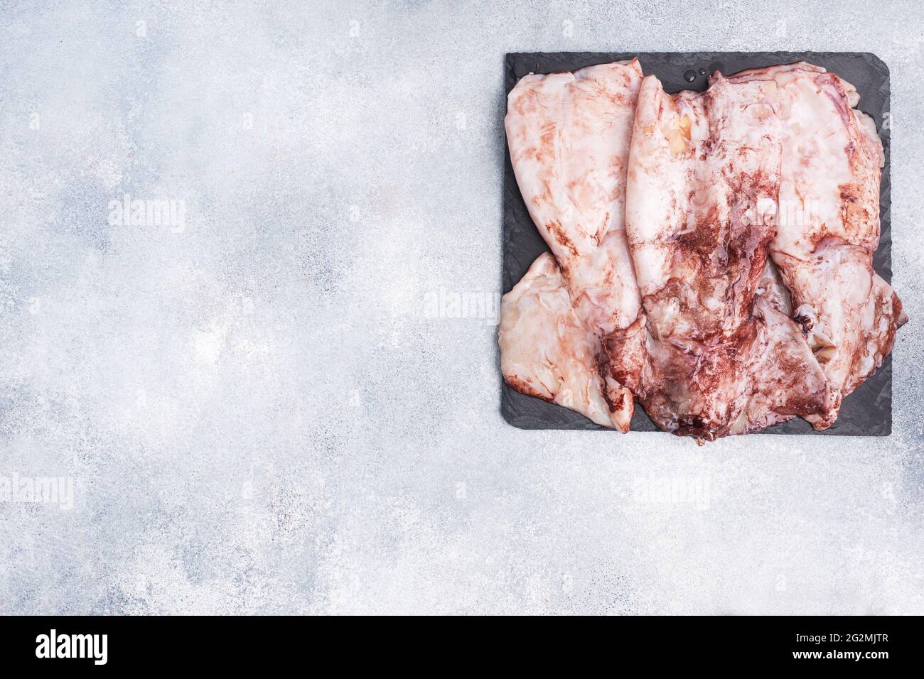Raw squid carcass with spices on a black slate board. copy space Top view Stock Photo