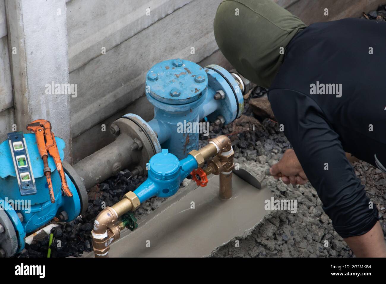 A plumber with balaclava works on an outdoor pipe for a condominium house Stock Photo