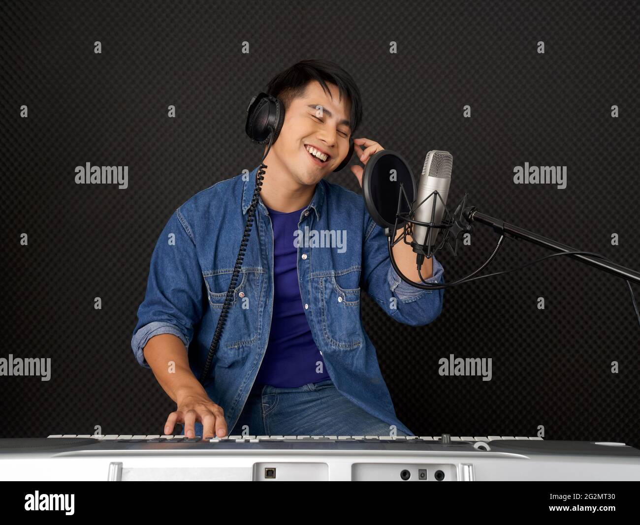 Young asian man with headphones playing an electric keyboard in front ...