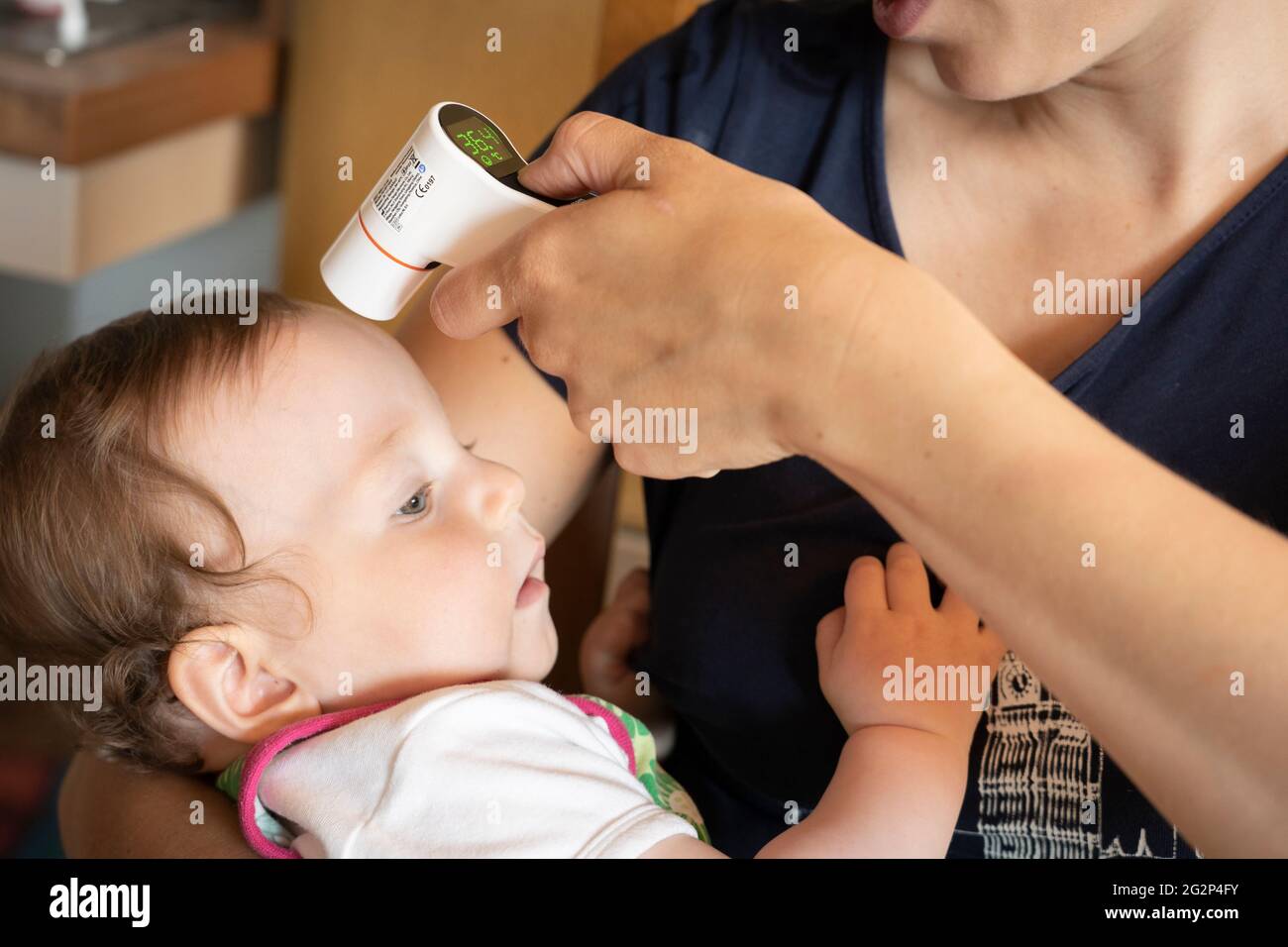 A mother worried about her baby daughter's health and taking her temperature using a digital infrared thermometer. UK Stock Photo
