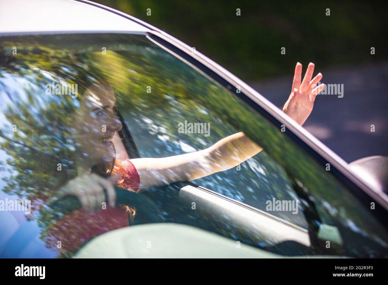 Motion blured image of happy young woman driving a car on a summer road trip travel vacations. Shot trough windshield. Stock Photo