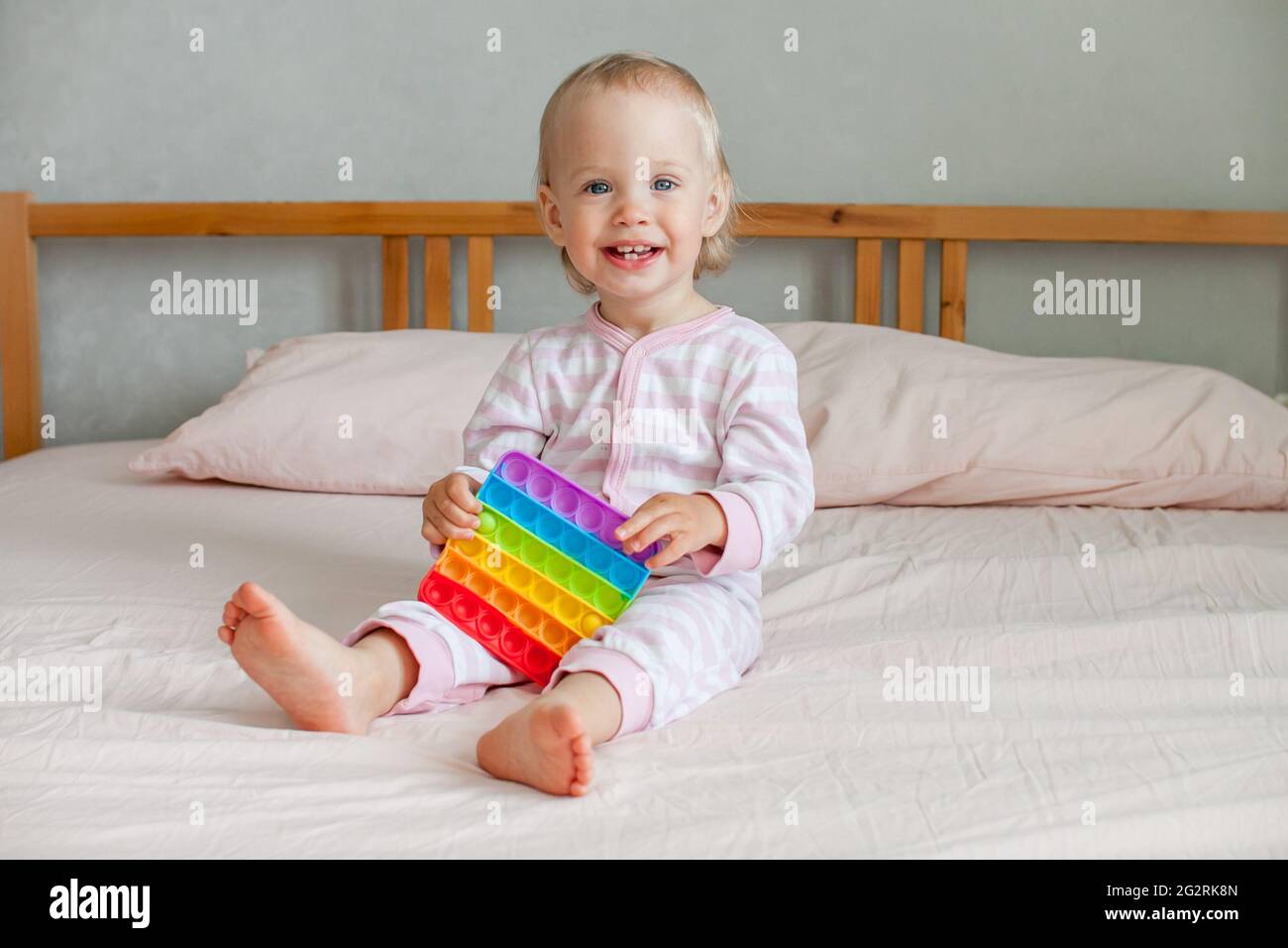 Little girl plays with trendy sensory toy pop it. The girl presses on colorful rainbow soft silicone bubbles. Relief of stress and anxiety. Stock Photo