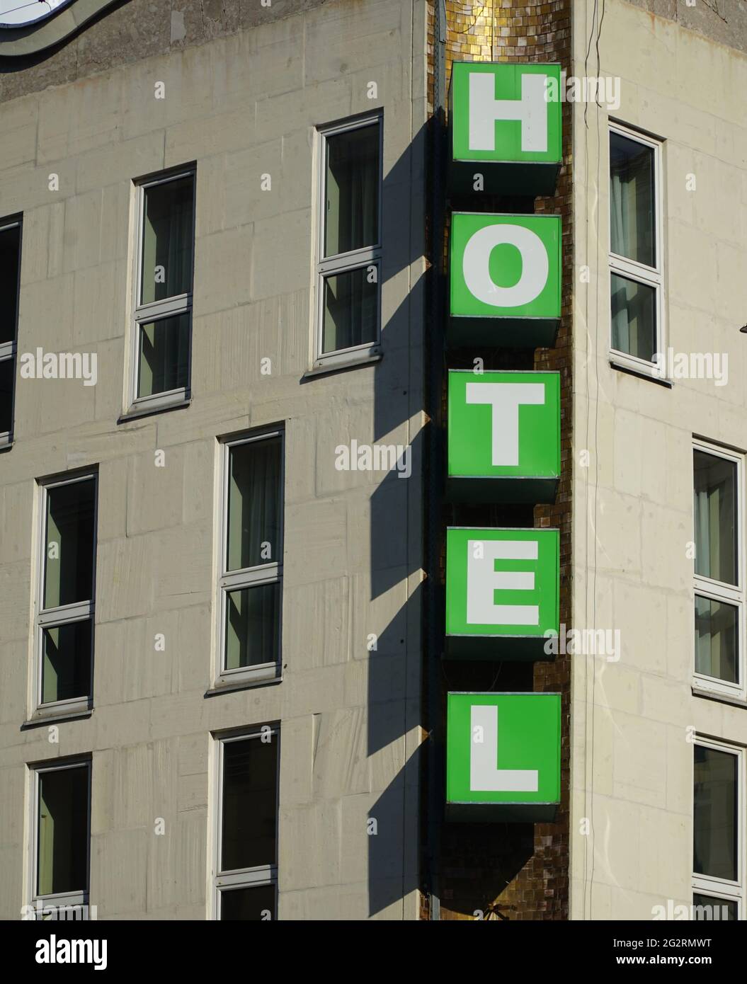 Vertical Hotel signboard over the entrance to the building. Vertical green hotel sign mounted on beige facade of hotel. White letters on green cubes. Stock Photo