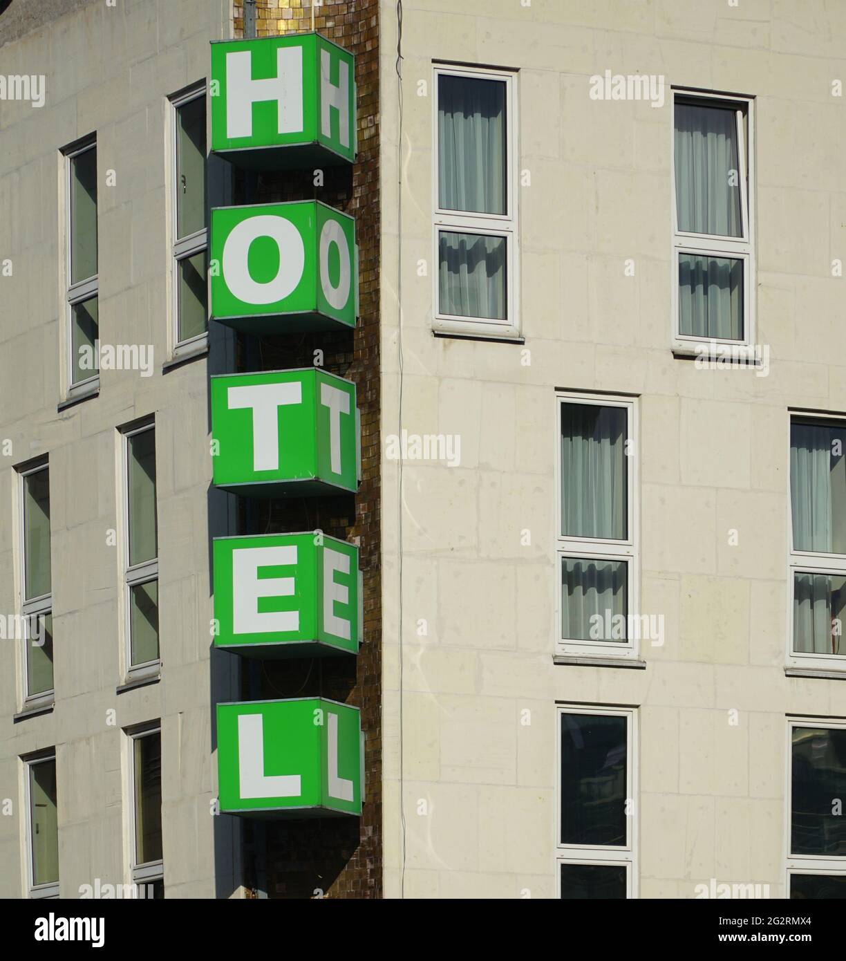 Vertical Hotel signboard over the entrance to the building. Vertical green hotel sign mounted on beige facade of hotel. White letters on green cubes. Stock Photo