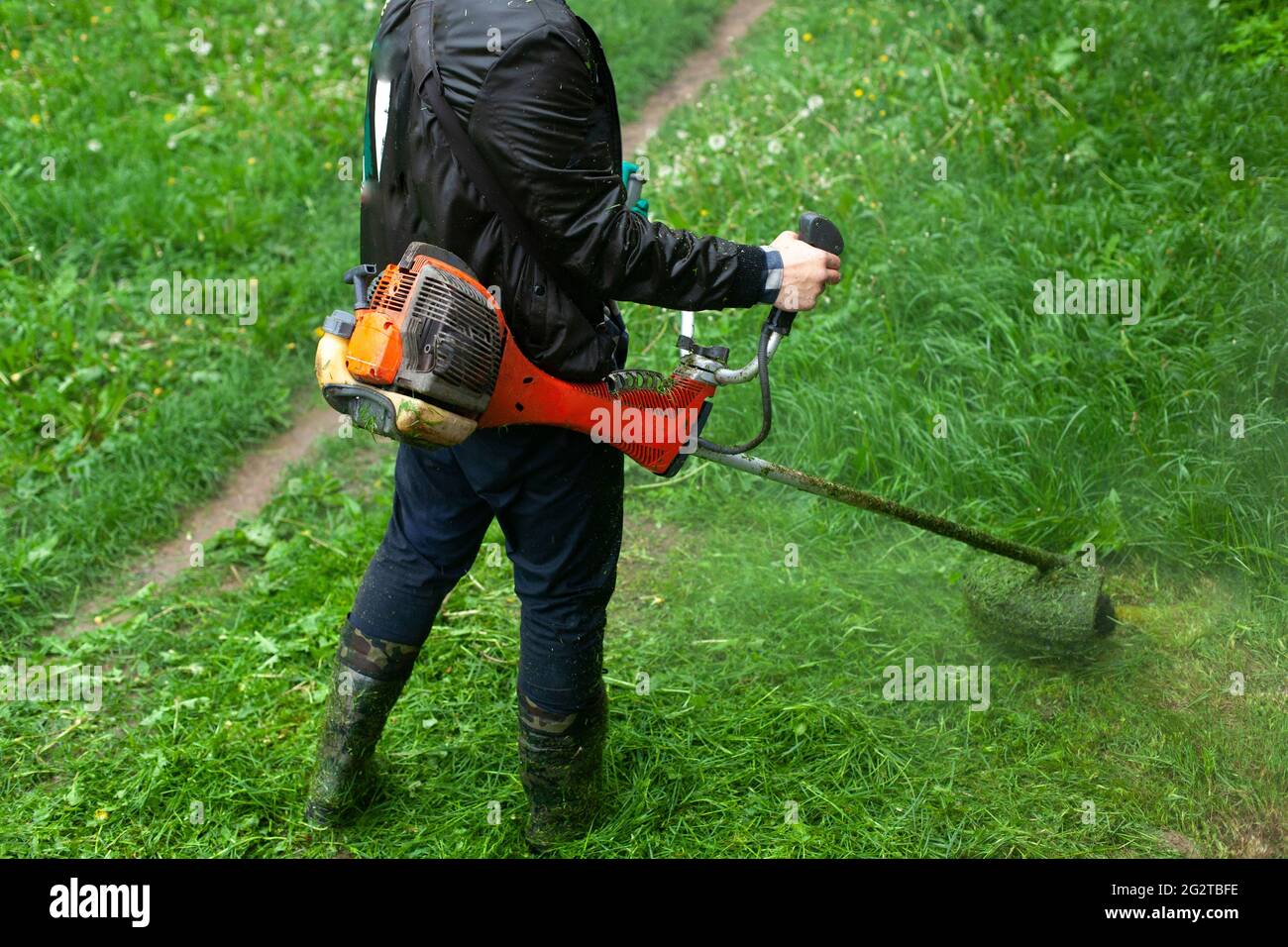 Mows the grass with a hand-held lawn mower. The gardener is cutting the lawn.  The gardener's tool cuts tall grass. The lawn mower in action Stock Photo -  Alamy