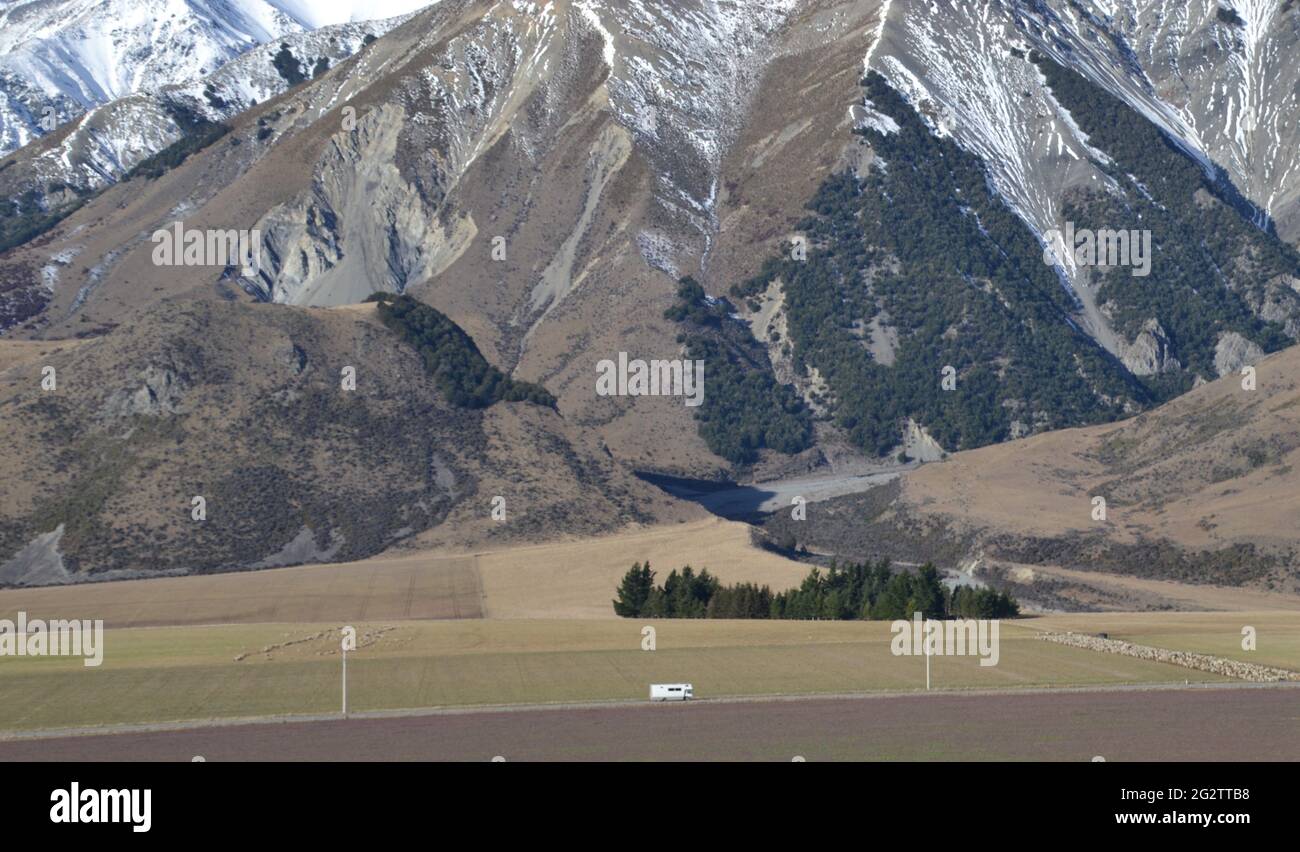 Tiny motorhome or RV in the distance at the foot of snowy slopes on New Zealand's South Island near Castle Hill also know as Ngai Tahu Kura Tawhiti Stock Photo