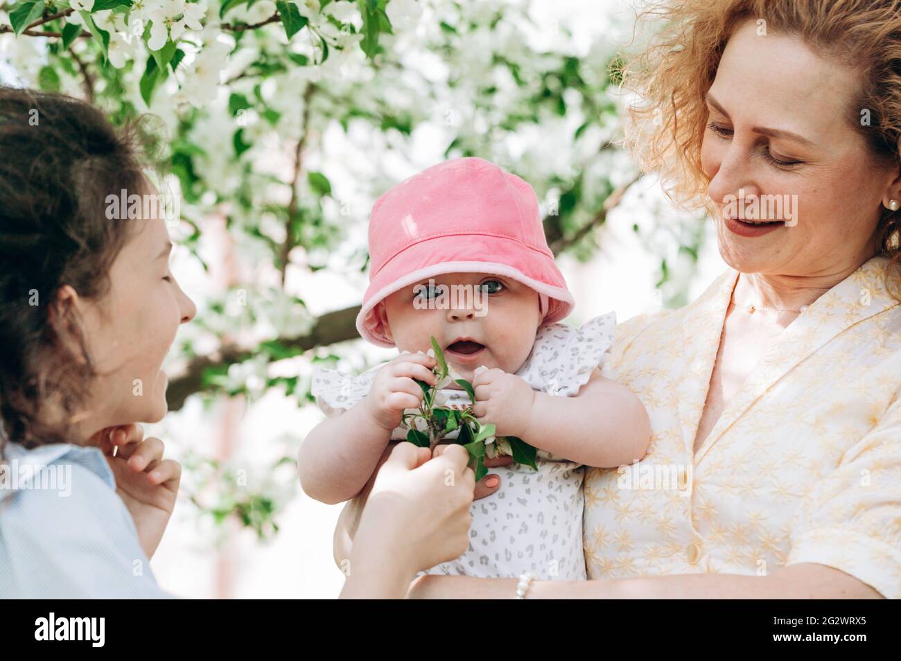 Happy family lifestyle photography. Smiling mom and her two happy cute daughters on a blooming spring garden. Childhood and motherhood concept. Green Stock Photo