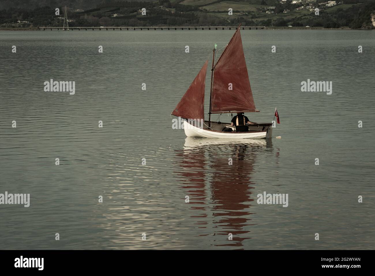 Traditional vintage style red sails on small yacht becalmed in bay. Stock Photo