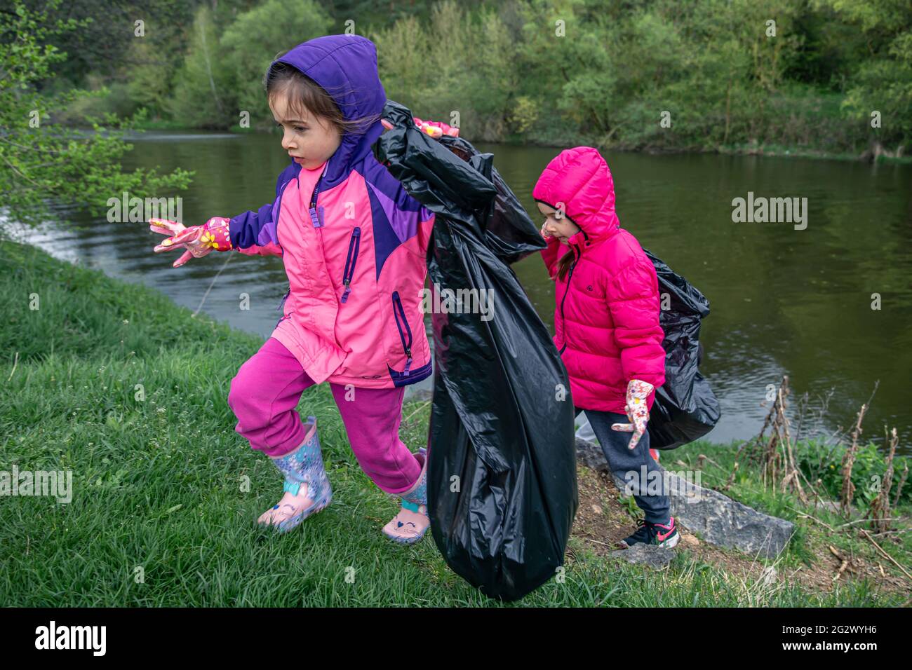 Two little girls with garbage bags in the forest are helping to clean up. Stock Photo