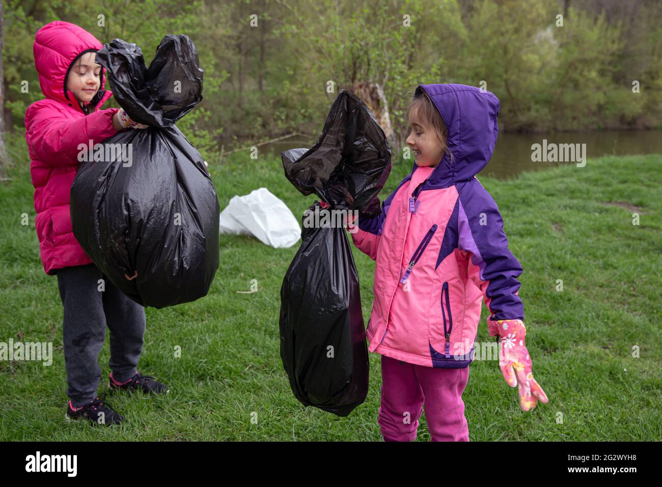Two little girls with garbage bags on a trip to nature, cleaning the environment. Stock Photo