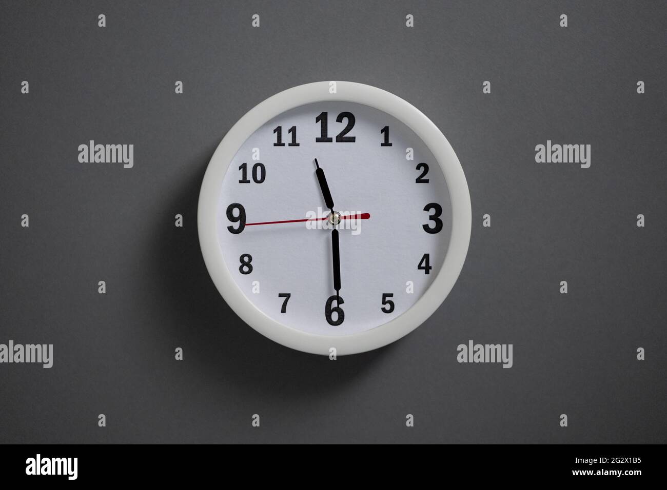 A white clock hangs on a gray wall. Stock Photo