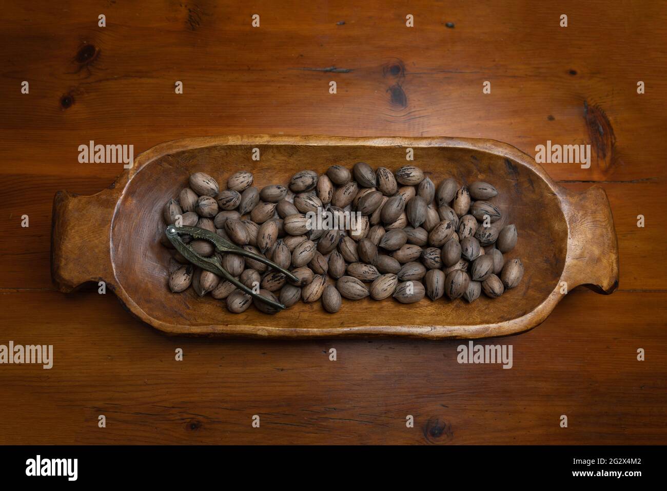 Raw in shell whole Pecan nuts in a wooden bowl on a wood table with a vintage nut cracker Stock Photo