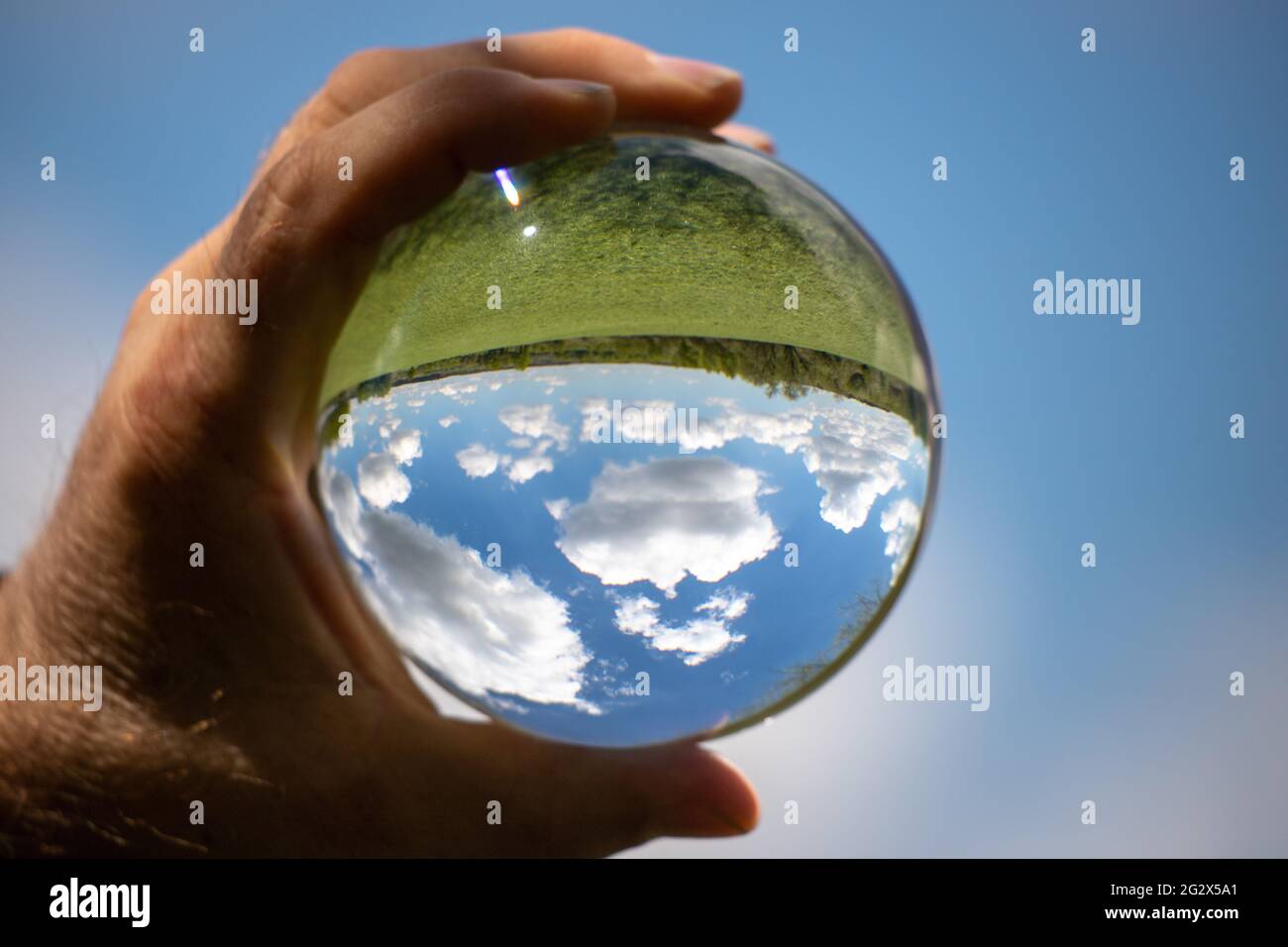 Landscape with green meadow and blue sky in a glass sphere held in the hand with defocused background Stock Photo