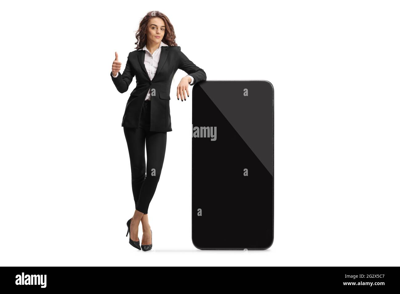 Full length portrait of a businesswoman leaning on a smartphone with empty screen and showing thumbs up isolated on white background Stock Photo